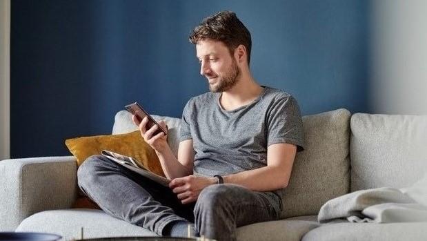 Mann i sofa som ser på mobilen sin.