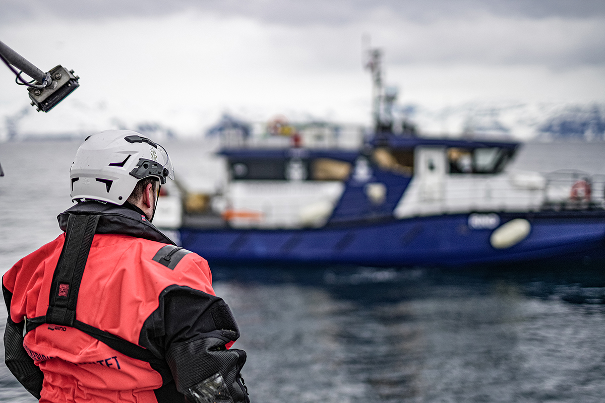 Figur 2.6 Inspektør frå Fiskeridirektoratets sjøteneste om bord ein reketrålar med kontrollfartøyet til sjøtenesta «Rind» i bakgrunnen.