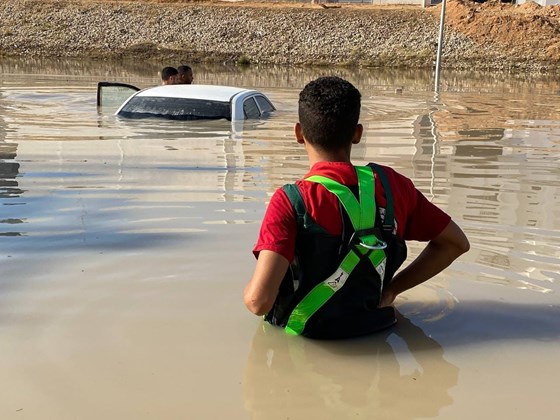 Bilde av bil under vann og redningsarbeider ved vannkanten under flommen i Libya