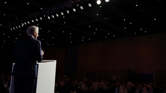 Statsministeren står ved en talerstol på scenen.