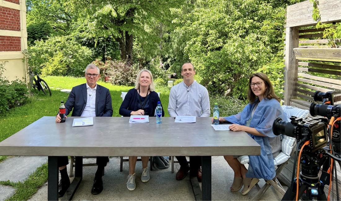 De fire deltakerne i panelsamtalen sitter rundt et stort, grått utebord i en frodig hage. Foto: NIM