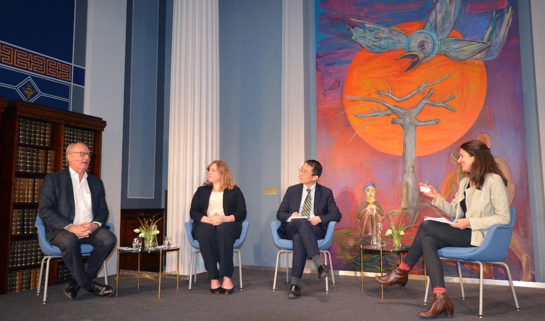 Fire paneldeltakere sitter på et podium foran et maleri av en fugl, et tre og en blodmåne. Maleriet er tipasset en nisje mellom to søyler i Domus Bibliotheca. Bildet heter Når gjøken bygger rede, og er malt av Bjørn Carlsen. Foto: Katrina Lavrinenko Friis-Olsen, UiO