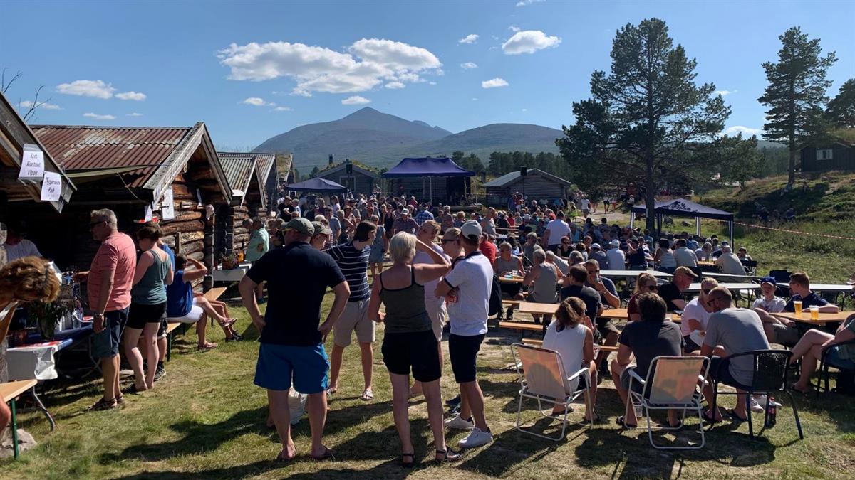 Mange personer på kulturarrangement på Fiskvollen, utenfor laftehus en fin sommerdag. Fjellområdet Sølen kan sees i bakgrunnen.