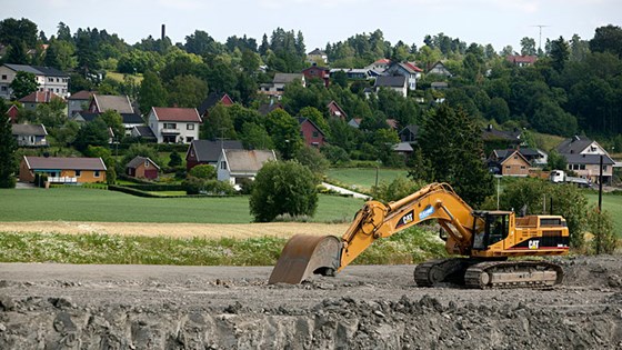 Gravemaskin på åker ved boligfelt.