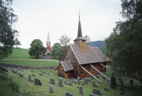 Figur 5.4 På 1800-tallet ble stavkirkene for små for
menighetene og mange ble revet når den nye kirken sto ferdig.
I Rødven står stavkirken fra ca 1300 og kirken
fra 1907 fremdeles side ved side. De iøynefallende skårdene
på stavkirken har en vindavsti...