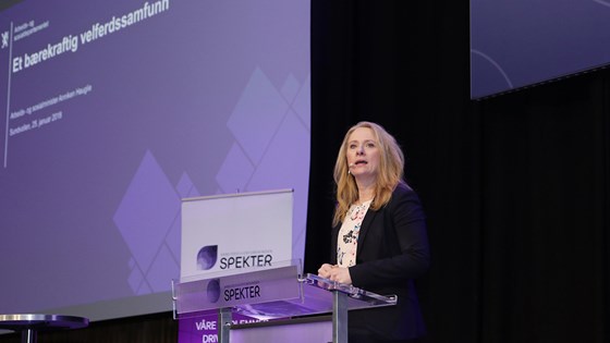 Arbeids- og sosialminister Anniken Hauglie på talerstol på Spekters vinterkonferanse 2018. Lerret med statsrådens presentasjon på bakveggen.