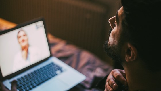 Nærbilde av en mann som ser på en dataskjerm der en lege gir e-konsultasjon. 