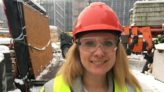 Nærebilde av Anniken Hauglie med rød vernehjelm og grønn refleksvest, på byggeplass