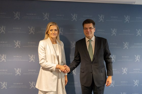 Woman in white suit shakes hands with man in dark suit in front of an official press wall