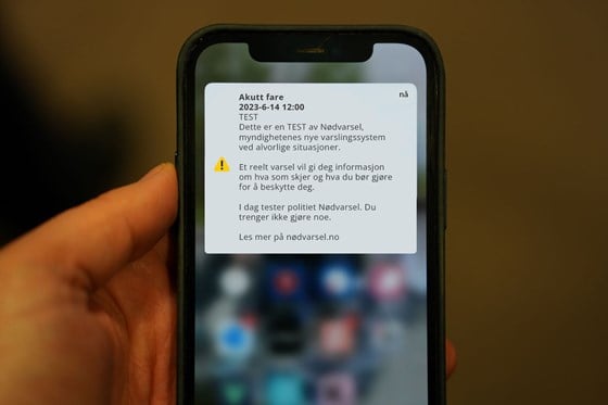 Hånd som holder en smartelefon med nødvarselmelding på skjermen