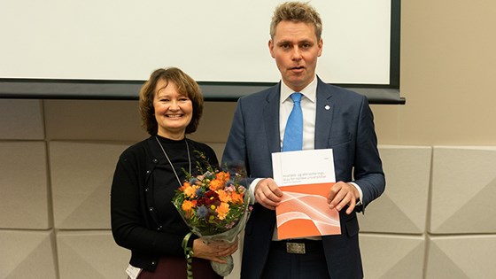 Bilde av Ingvild Marheim Larsen, leder av akkrediteringsutvalget med blomster og forsknings- og høyere utdanningsminister Ola Borten Moe som holder rapporten.