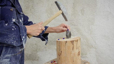 Ser hendene til kunstner som deler en liten blå glasstein med hammer.