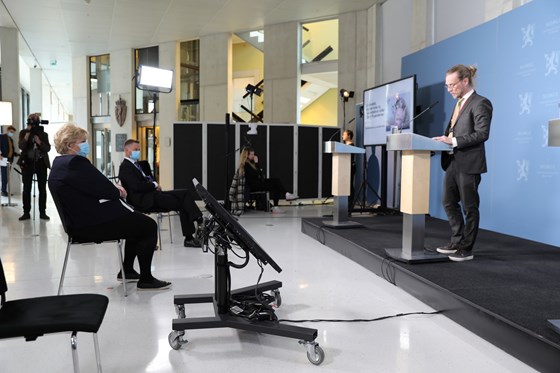 Peder Kjøs står ved talerstol på scenen og snakker bla. til statsminister Erna Solberg og helse- og omsorgsminister Bent Høie.