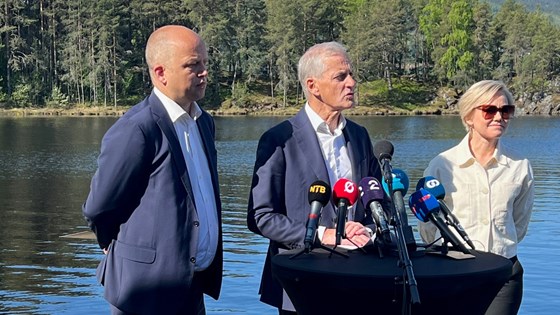 Statsminister Jonas Gahr Støre, finansminister Trygve Slagsvold Vedum og helse- og omsorgsminister Ingvild Kjerkol står på en brygge med vann og skog i bakgrunnen.