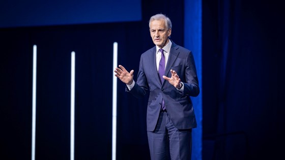 Statsminister Jonas Gahr Støre står på scenen i Oslo Spektrum. Dress med lilla slips.