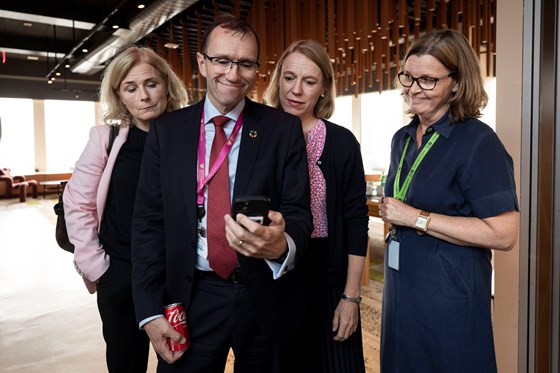 Bilde av Barth Eide som viser noe på telefonen til tre andre, stående