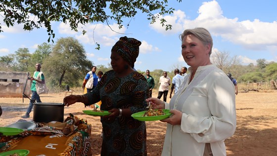 WFP/Ana Hombre Bilde av Anne Beathe Tvinnereim sammen med person som serverer skolemat utendørs under et tre
