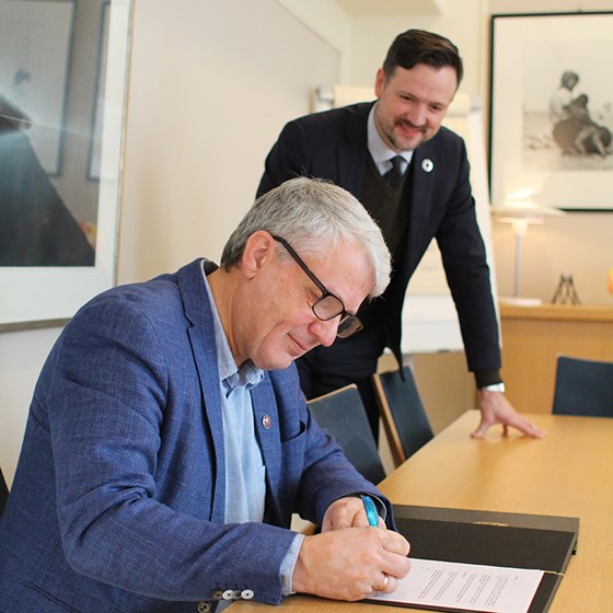 Generalsekretær Dagfinn Høybråten i Kirkens Nødhjelp signerer samarbeidsavtalen med Utenriksdepartementet. En fornøyd giver og utviklingsminister ser til at det går riktig for seg. Foto: Sondre Olsen, UD